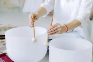 Hands playing crystal singing bowls with mallets, highlighting sound healing practice indoors.