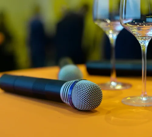 Close-up of microphones and wine glasses on an orange table, ideal for events or entertainment themes.