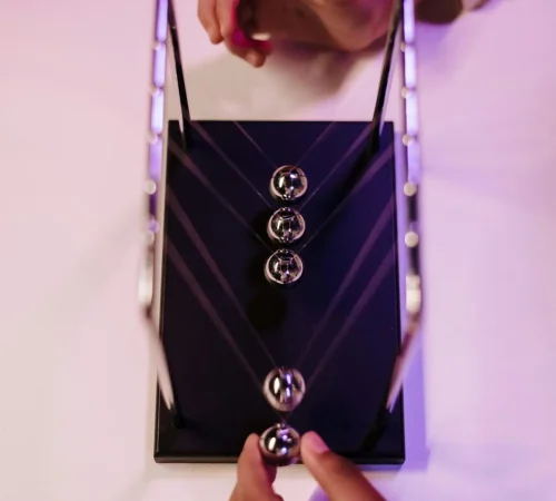 A close-up view of a Newton's cradle being activated by hands showcasing physics in motion.